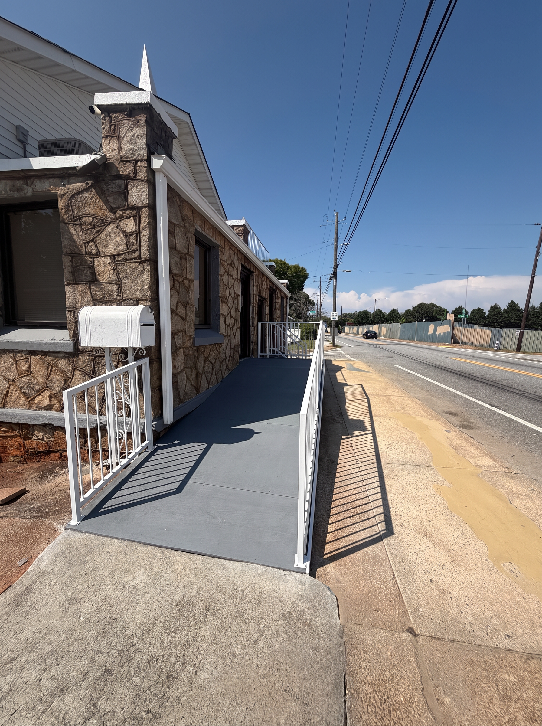 Completed ramp with a freshly sealed gray walkway beside a stone building