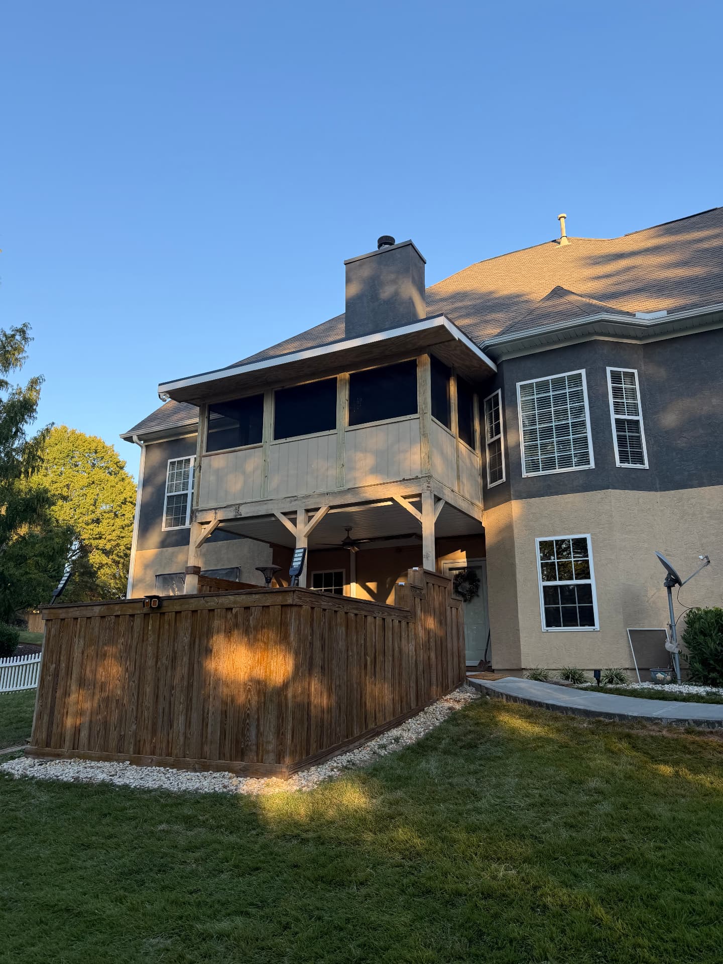 Finished two-story screened porch with wooden fencing and a stone bed beside a gray home