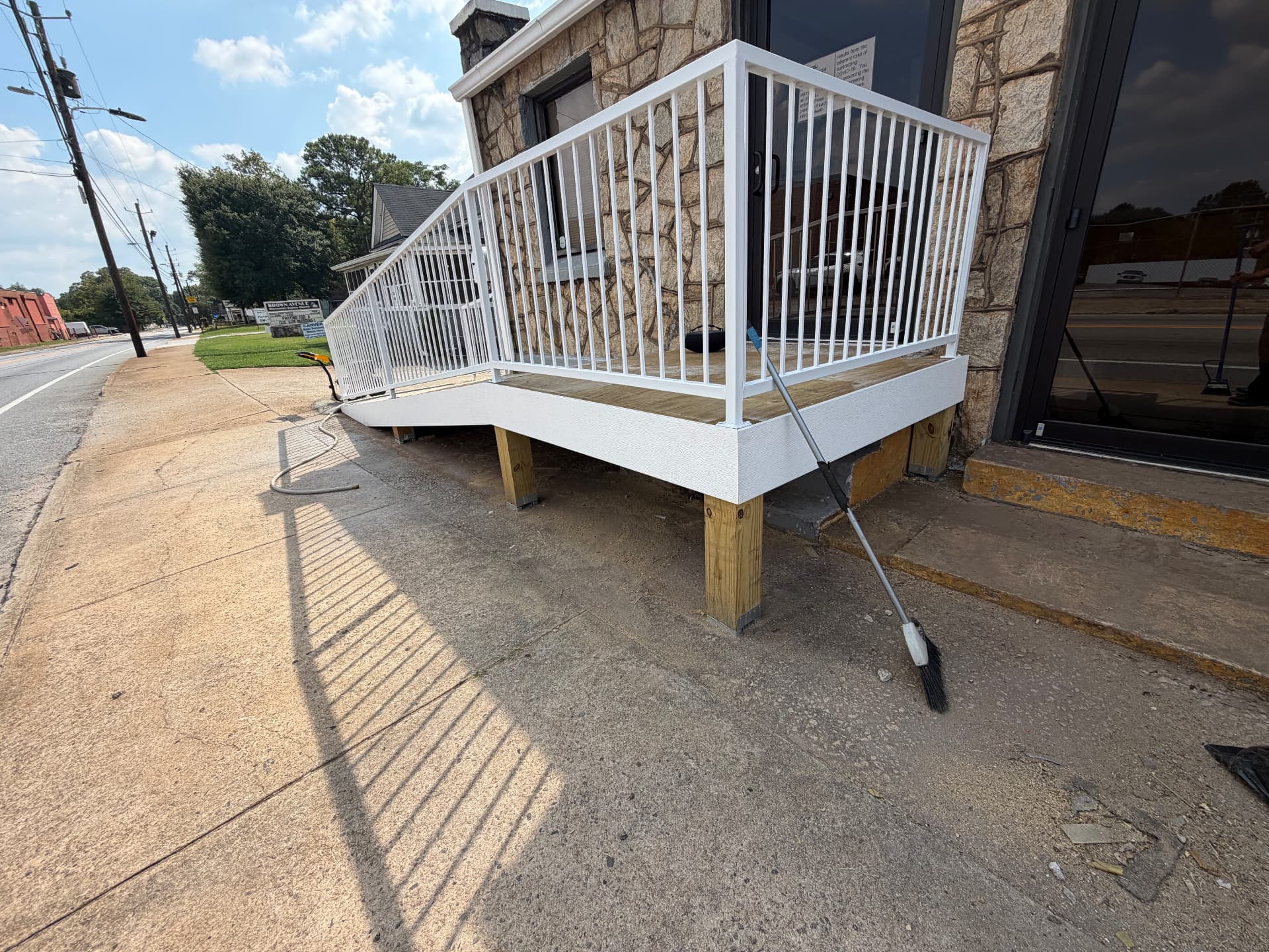 Finished wooden ramp with white metal railings wrapping around an entrance