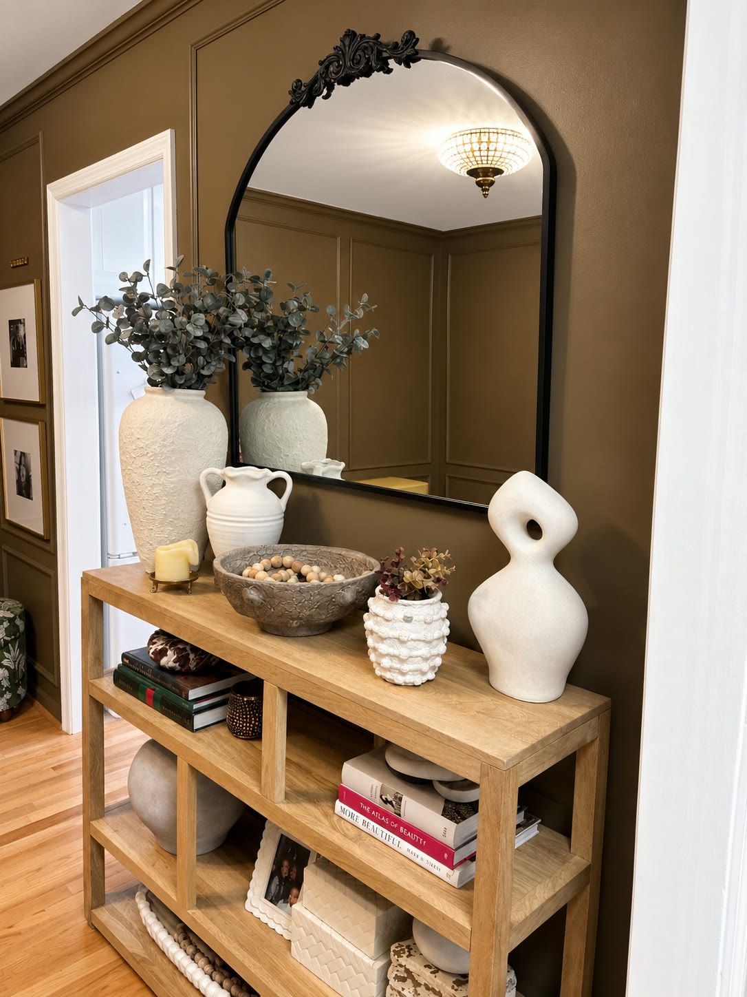 Styled finished room with warm brown paneled walls, an arched mirror and a wooden console table