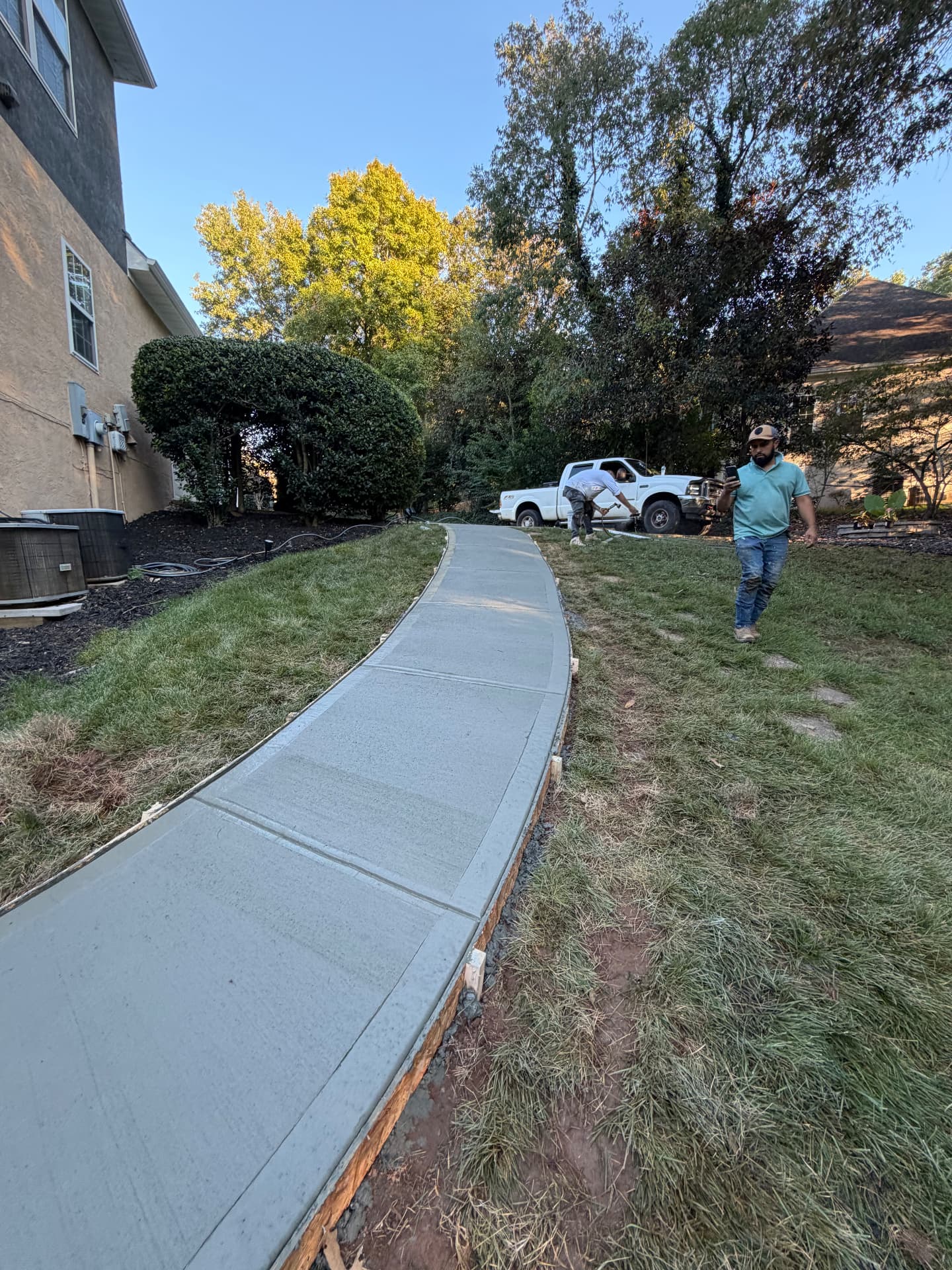 Finished concrete walkway curving through a grassy backyard beside a home