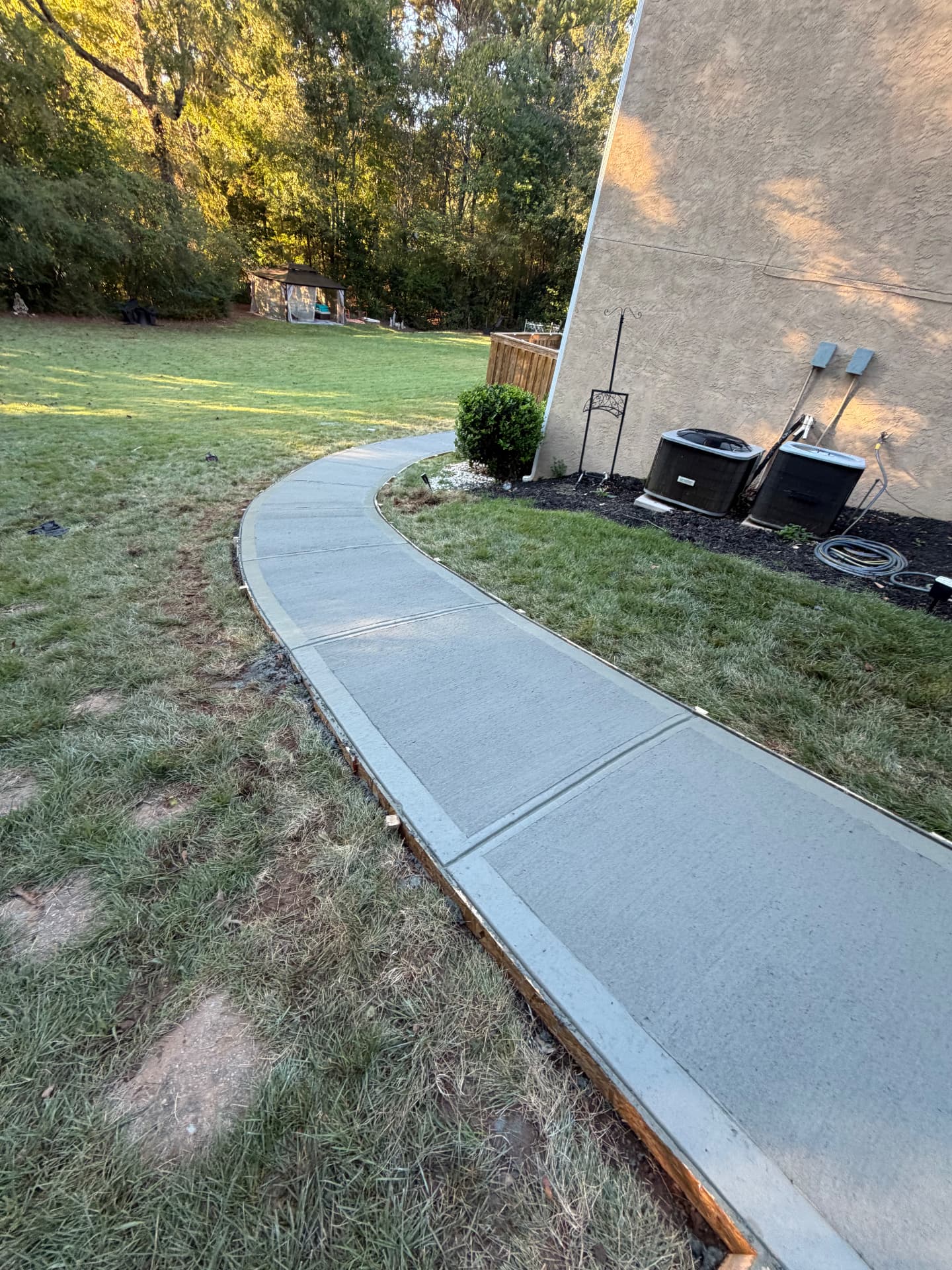 Finished curved concrete walkway winding through a sunny backyard